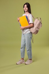 Photo of Cute teenage girl with backpack and books on olive background