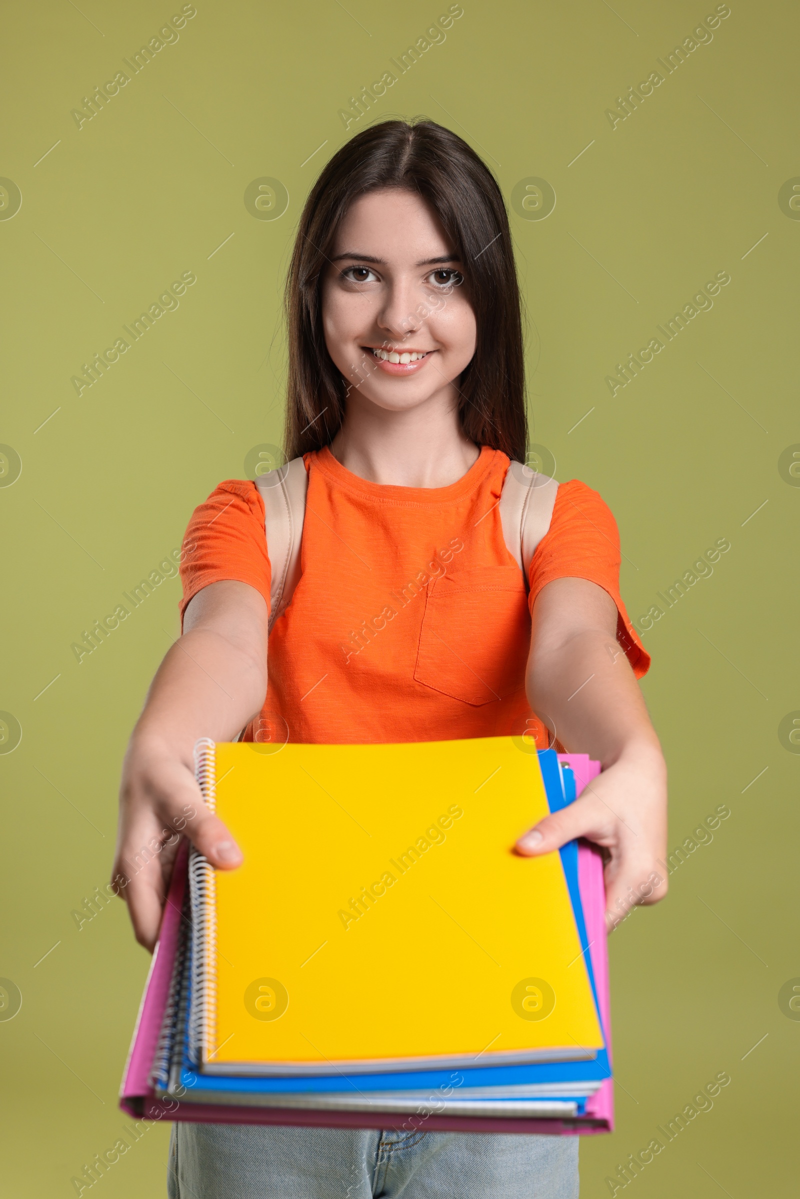 Photo of Cute teenage girl with backpack holding books on olive background