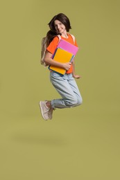 Photo of Cute teenage girl with backpack and books jumping on olive background