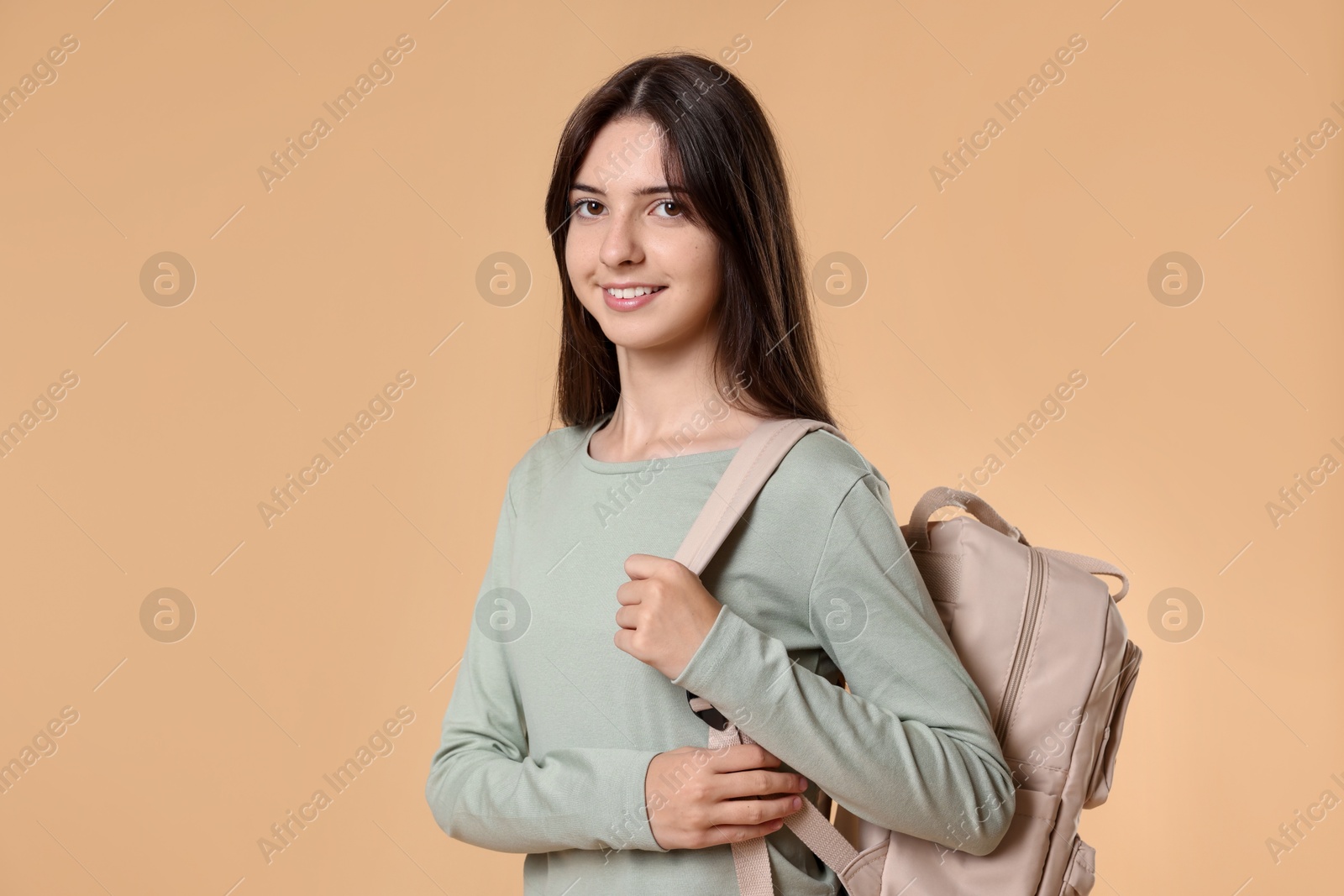 Photo of Portrait of smiling teenage girl with backpack on beige background