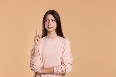 Portrait of cute teenage girl pointing at something on beige background. Space for text