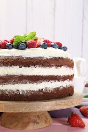 Delicious chocolate sponge cake with berries and mint on pink wooden table, closeup