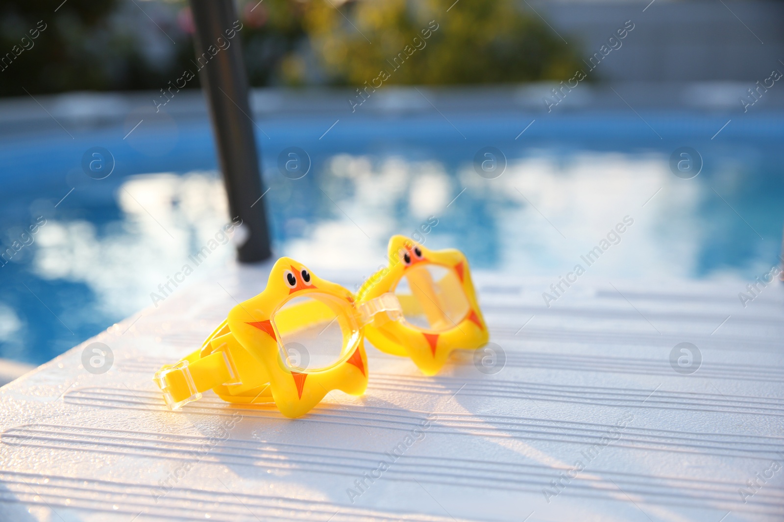 Photo of Yellow swimming goggles for kids on ladder outdoors, closeup. Space for text