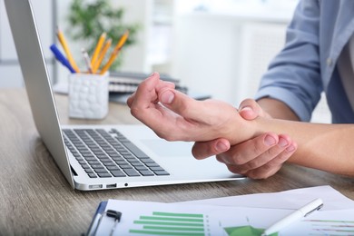 Photo of Man suffering from pain in wrist while working on laptop at table indoors, closeup. Carpal tunnel syndrome