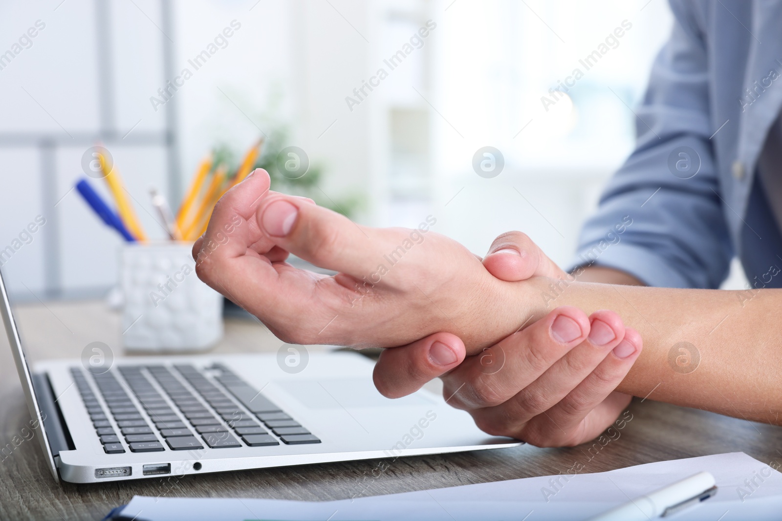 Photo of Man suffering from pain in wrist while working on laptop at table indoors, closeup. Carpal tunnel syndrome