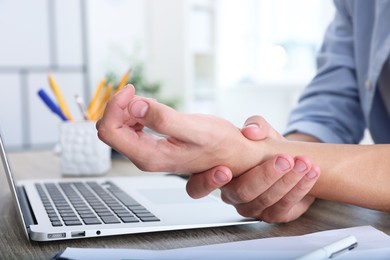 Photo of Man suffering from pain in wrist while working on laptop at table indoors, closeup. Carpal tunnel syndrome