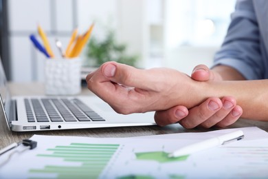 Photo of Man suffering from pain in wrist while working on laptop at table indoors, closeup. Carpal tunnel syndrome