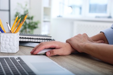 Photo of Man suffering from pain in wrist while using computer mouse at table indoors, closeup. Carpal tunnel syndrome