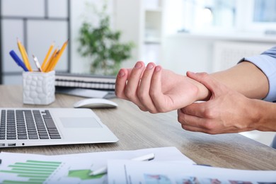 Photo of Man suffering from pain in wrist while working on laptop at table indoors, closeup. Carpal tunnel syndrome