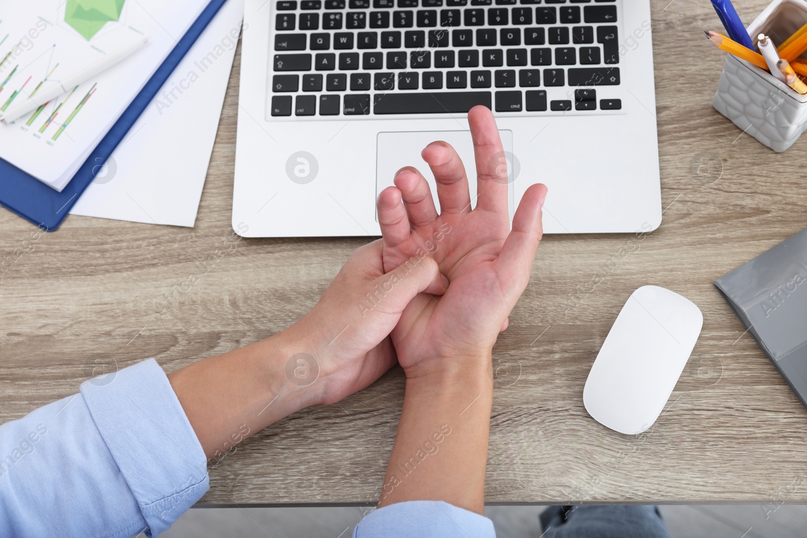 Photo of Man suffering from pain in wrist while working on laptop at wooden table, closeup, top view. Carpal tunnel syndrome