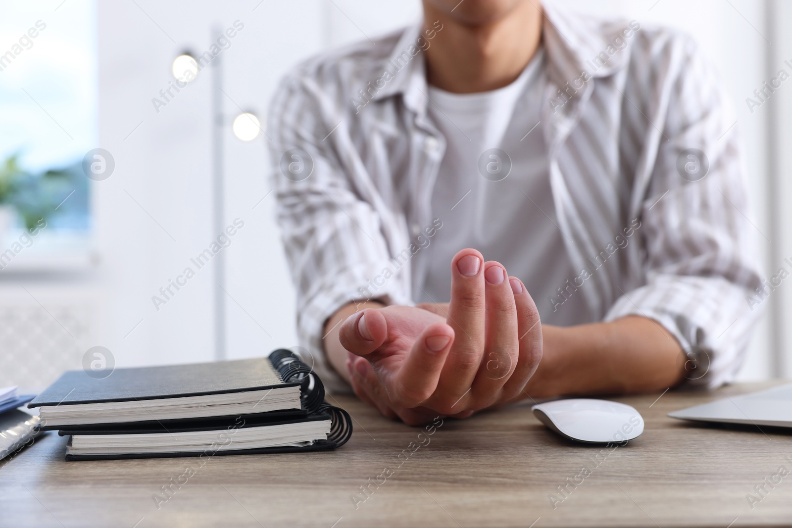 Photo of Man suffering from pain in wrist while working on laptop at table indoors, closeup. Carpal tunnel syndrome