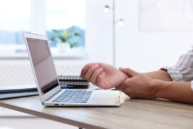 Photo of Man suffering from pain in wrist while working on laptop at table indoors, closeup. Carpal tunnel syndrome