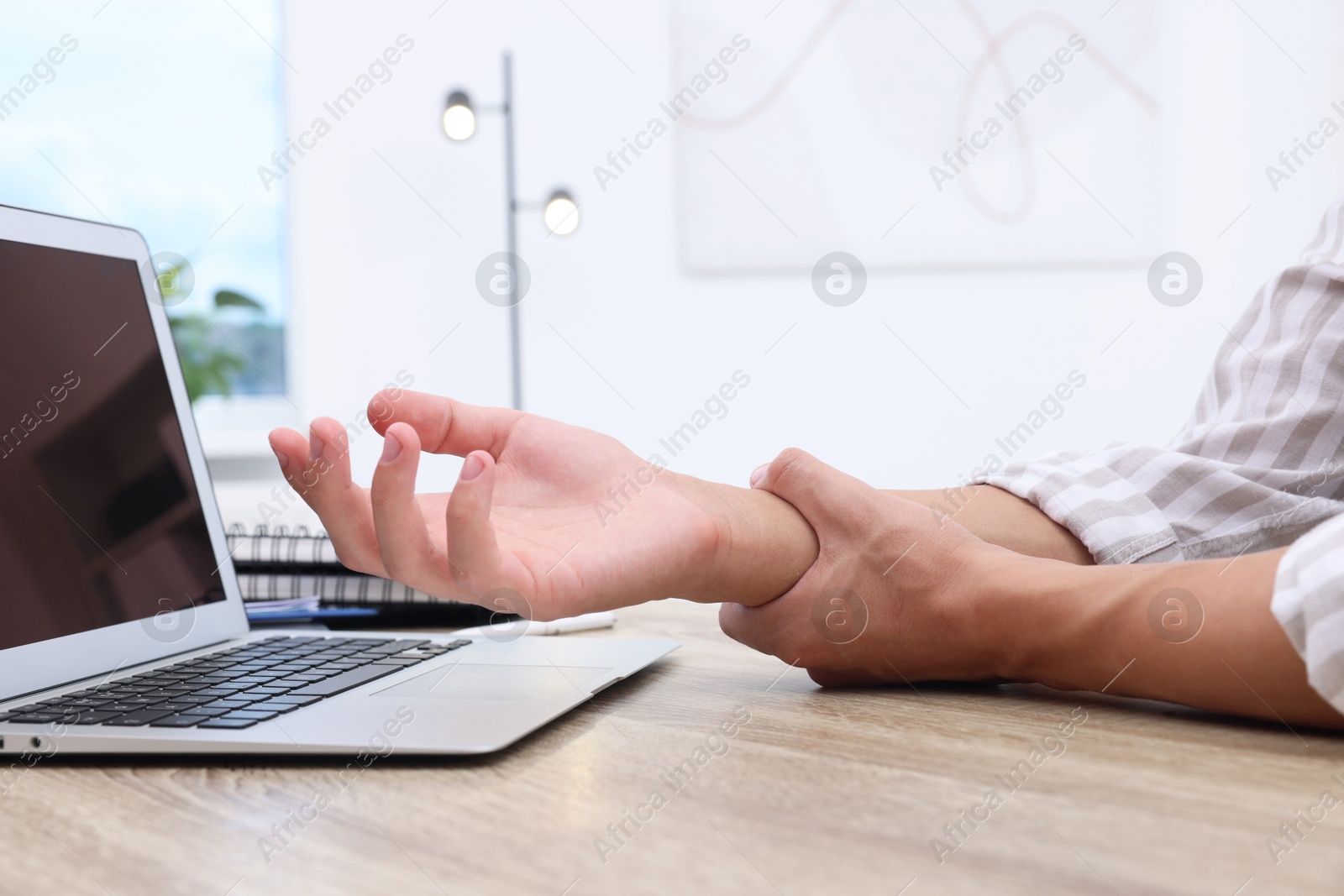 Photo of Man suffering from pain in wrist while working on laptop at table indoors, closeup. Carpal tunnel syndrome