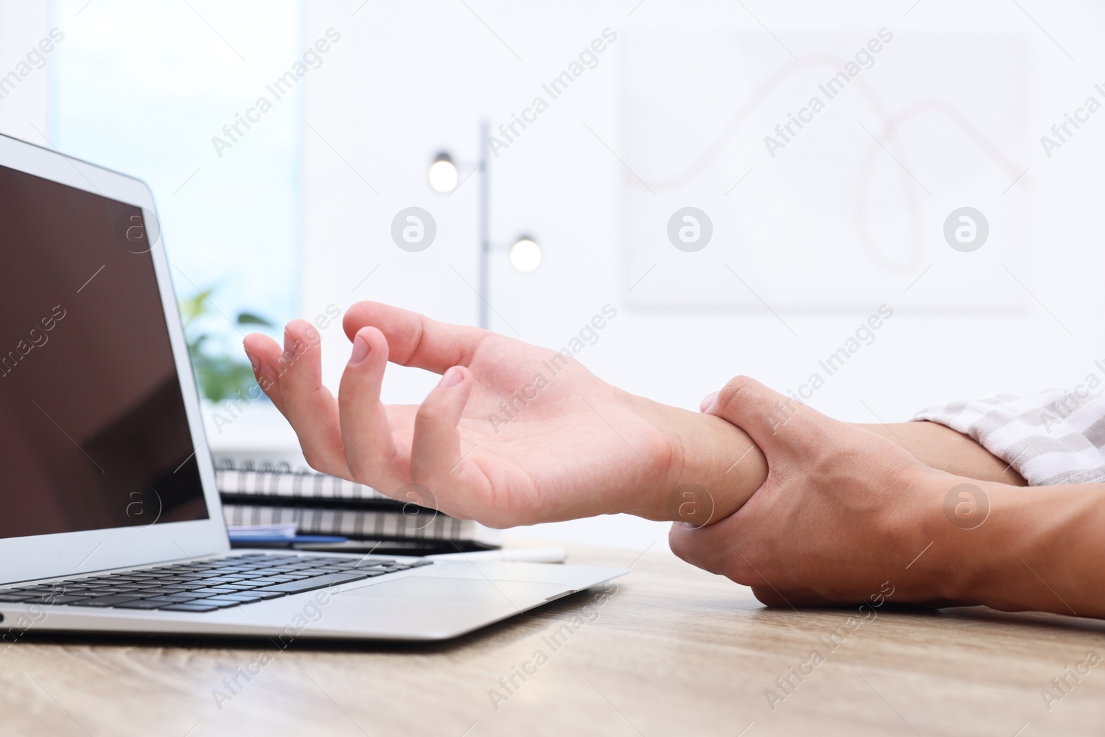 Photo of Man suffering from pain in wrist while working on laptop at table indoors, closeup. Carpal tunnel syndrome