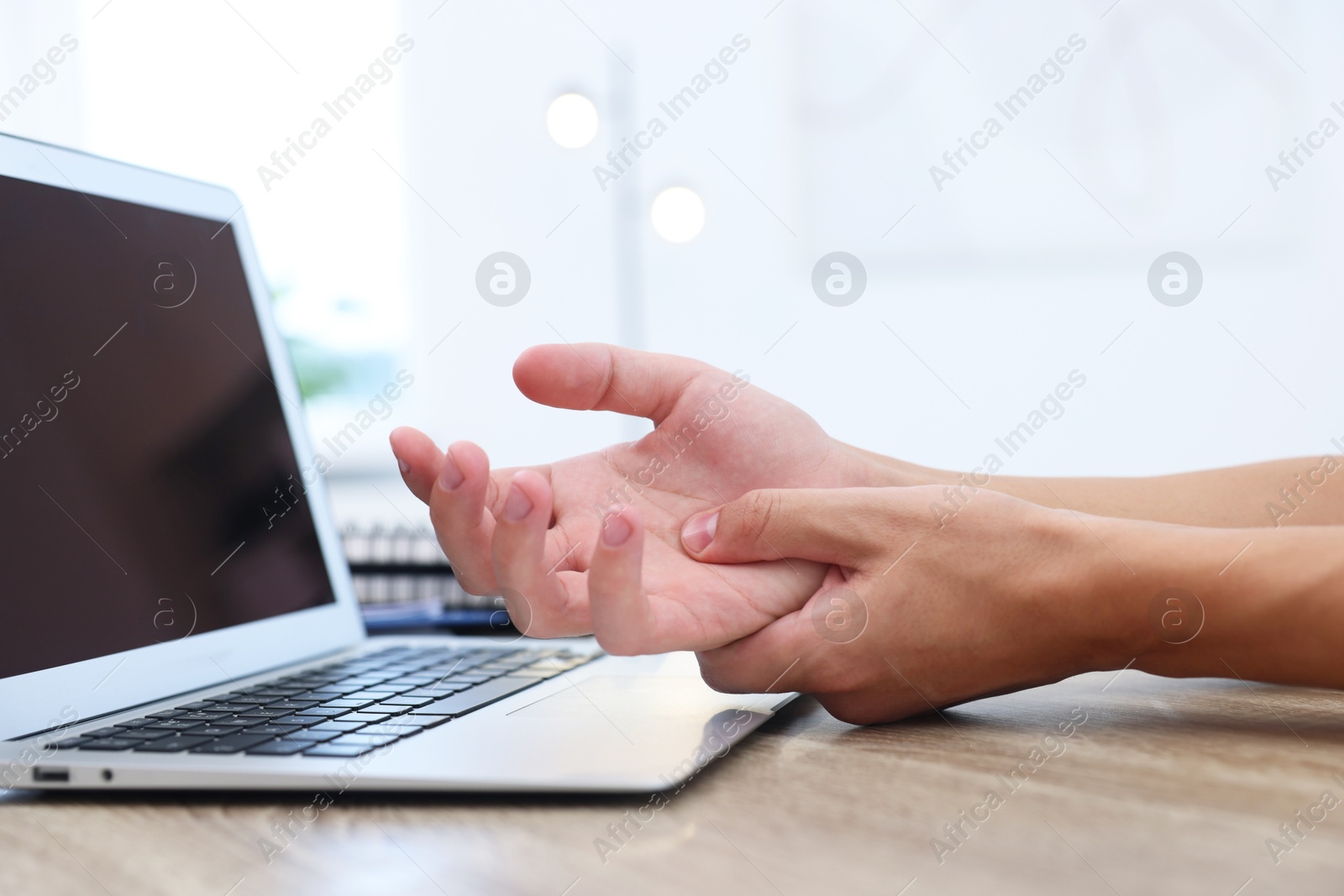 Photo of Man suffering from pain in wrist while working on laptop at table indoors, closeup. Carpal tunnel syndrome