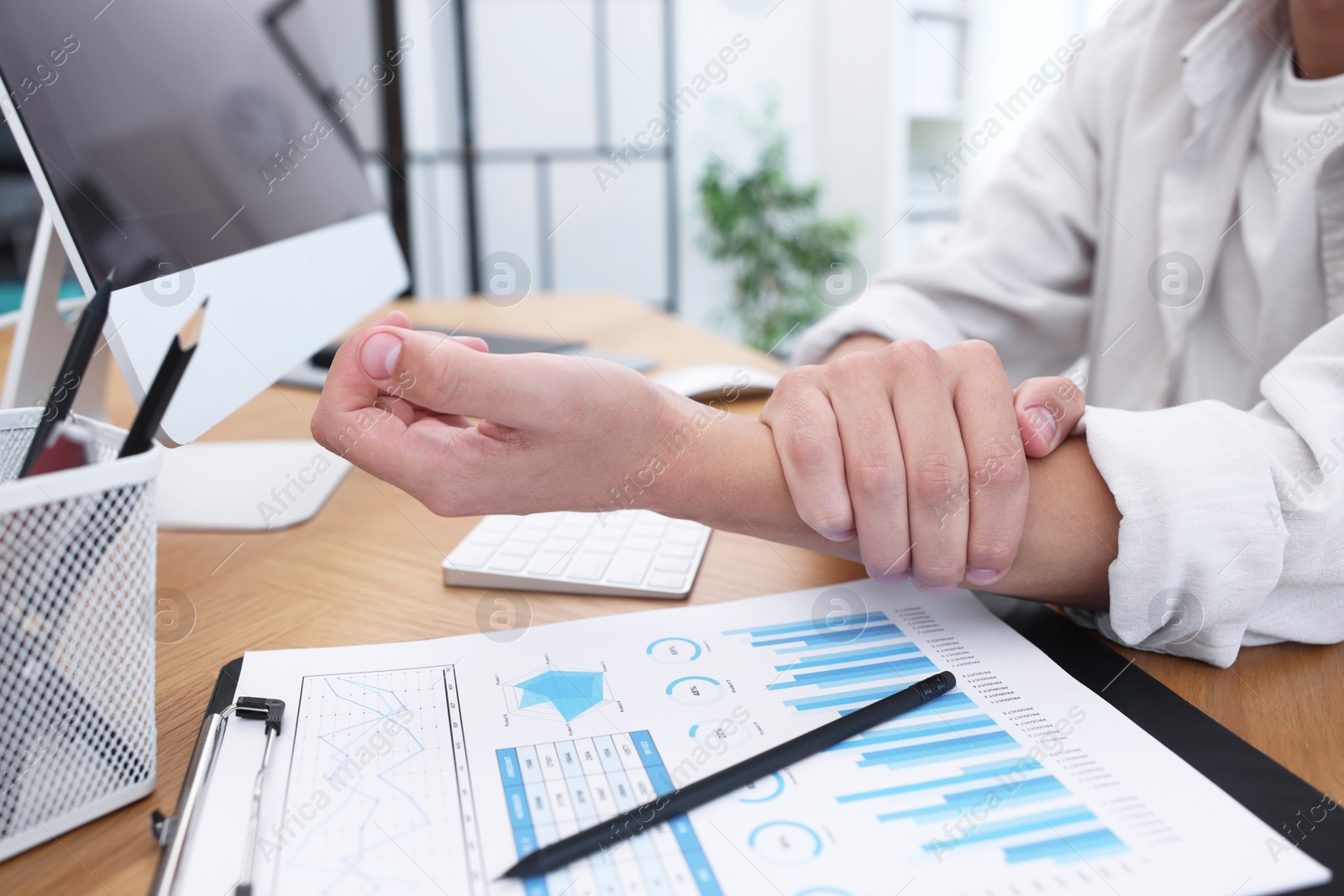 Photo of Man suffering from pain in wrist while working on computer at table indoors, closeup. Carpal tunnel syndrome