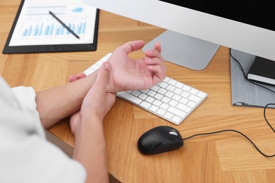 Photo of Man suffering from pain in wrist while working on computer at wooden table, closeup. Carpal tunnel syndrome