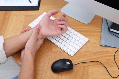 Photo of Man suffering from pain in wrist while working on computer at wooden table, closeup. Carpal tunnel syndrome