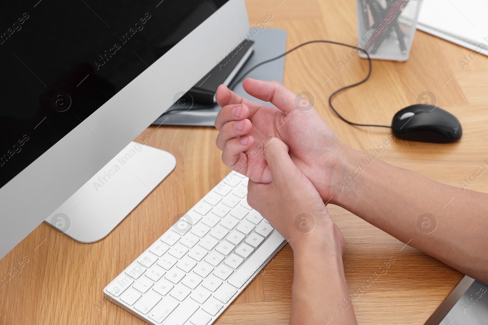 Photo of Man suffering from pain in wrist while working on computer at wooden table, closeup. Carpal tunnel syndrome