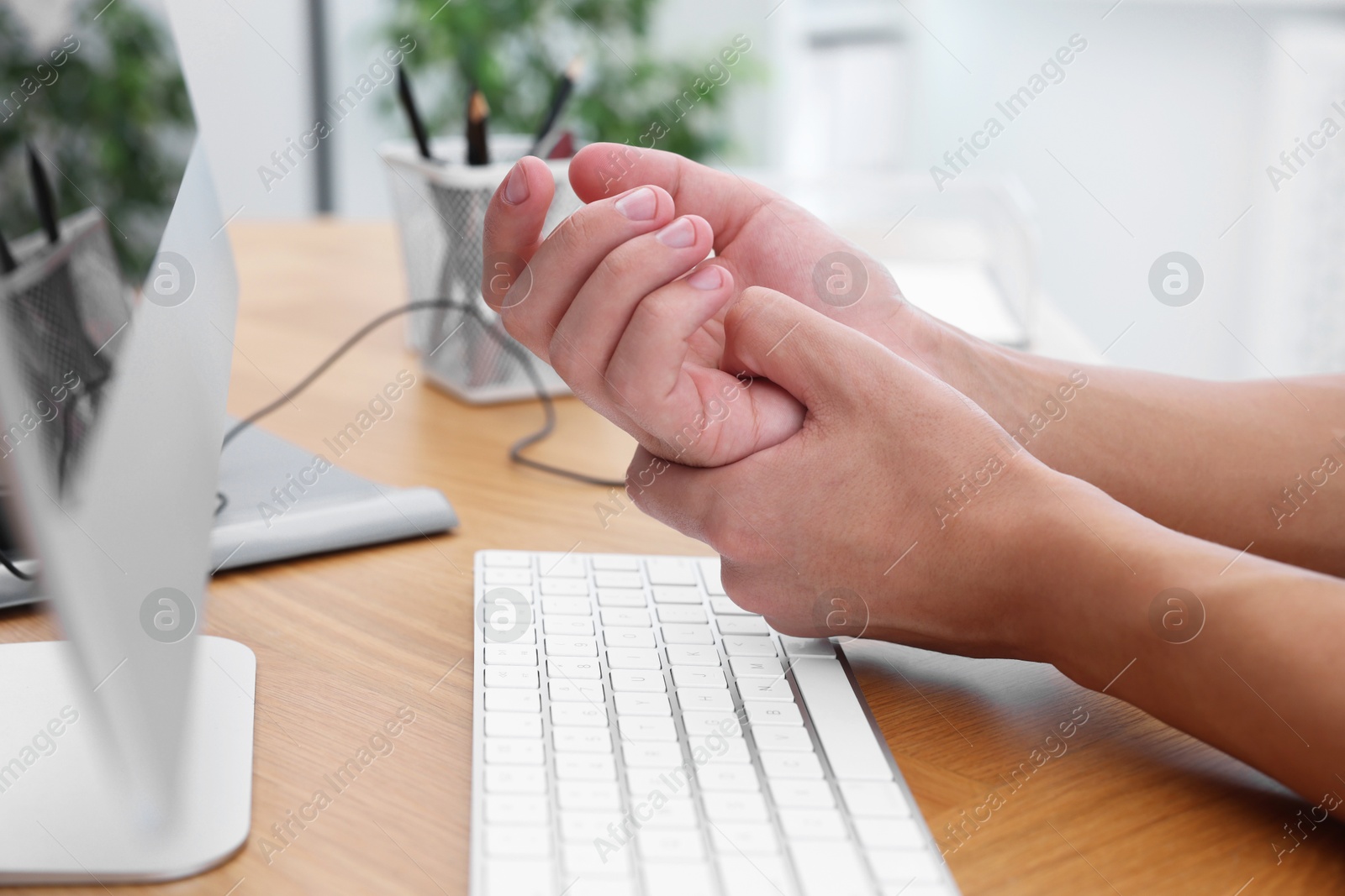 Photo of Man suffering from pain in wrist while working on computer at table indoors, closeup. Carpal tunnel syndrome