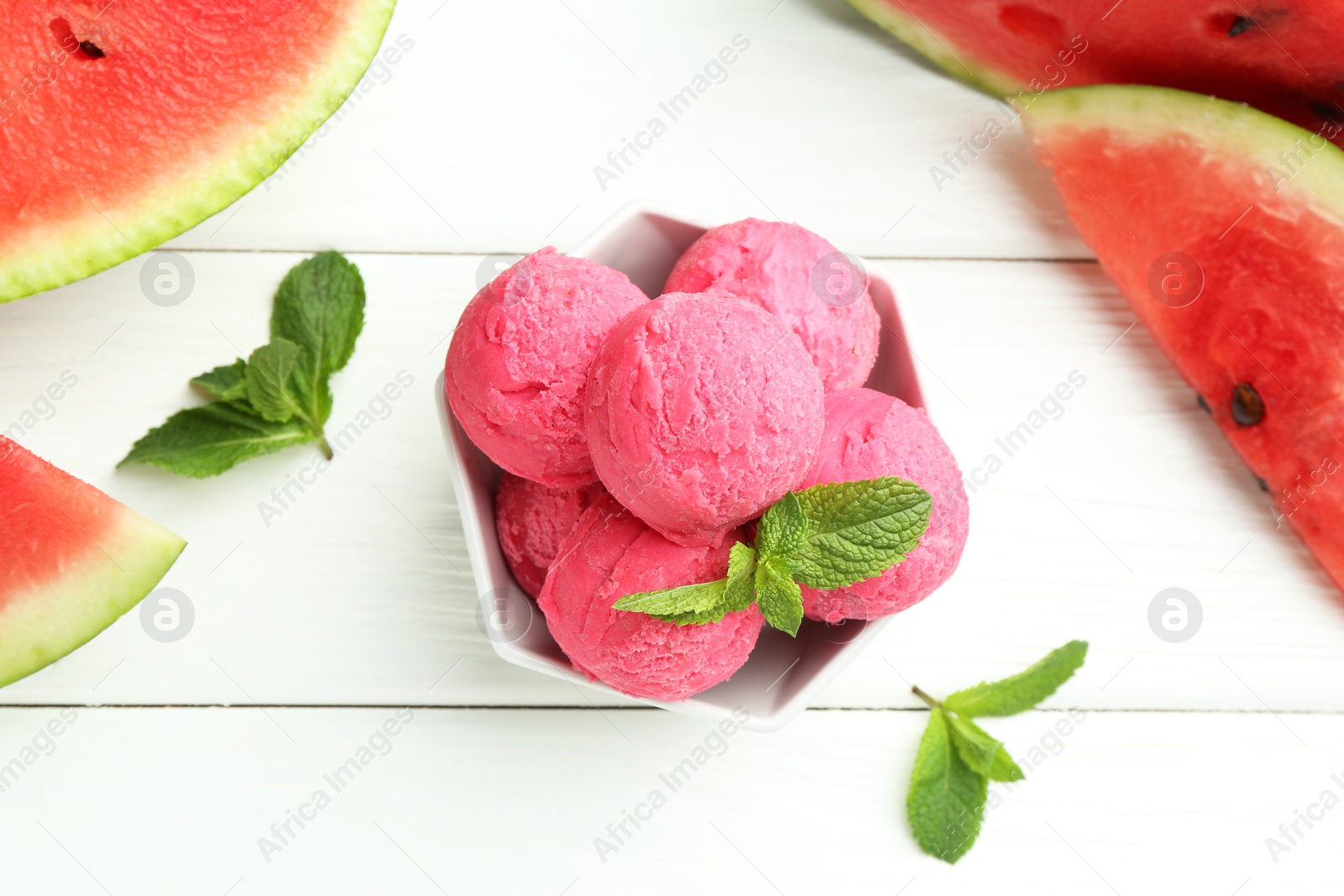 Photo of Scoops of tasty watermelon sorbet with mint in bowl and fresh fruit on white wooden table, flat lay