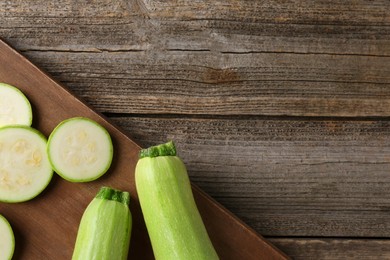 Photo of Board with fresh zucchinis on wooden table, top view. Space for text