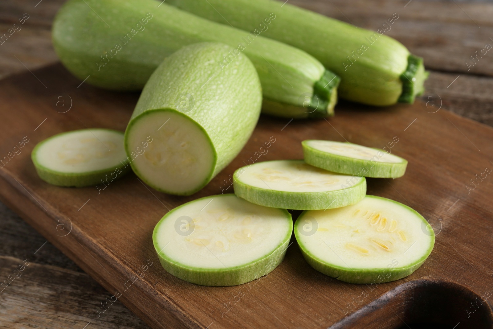 Photo of Board with fresh zucchinis on wooden table, closeup