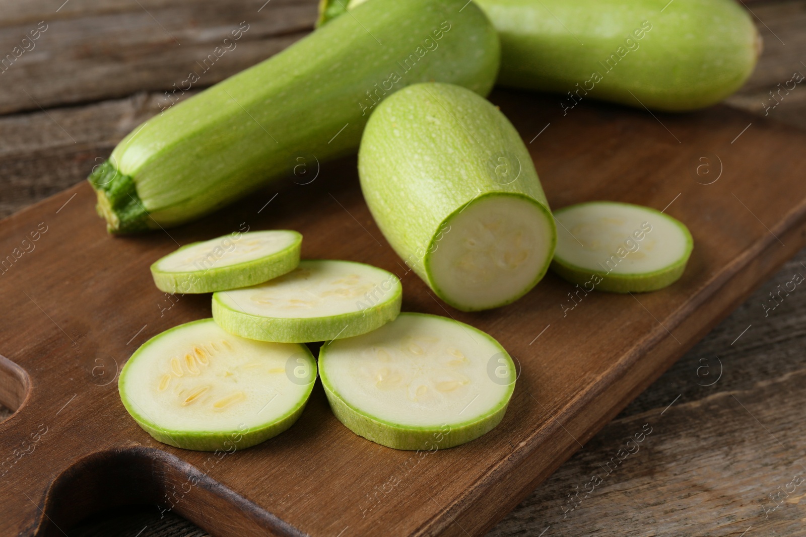 Photo of Board with fresh zucchinis on wooden table, closeup