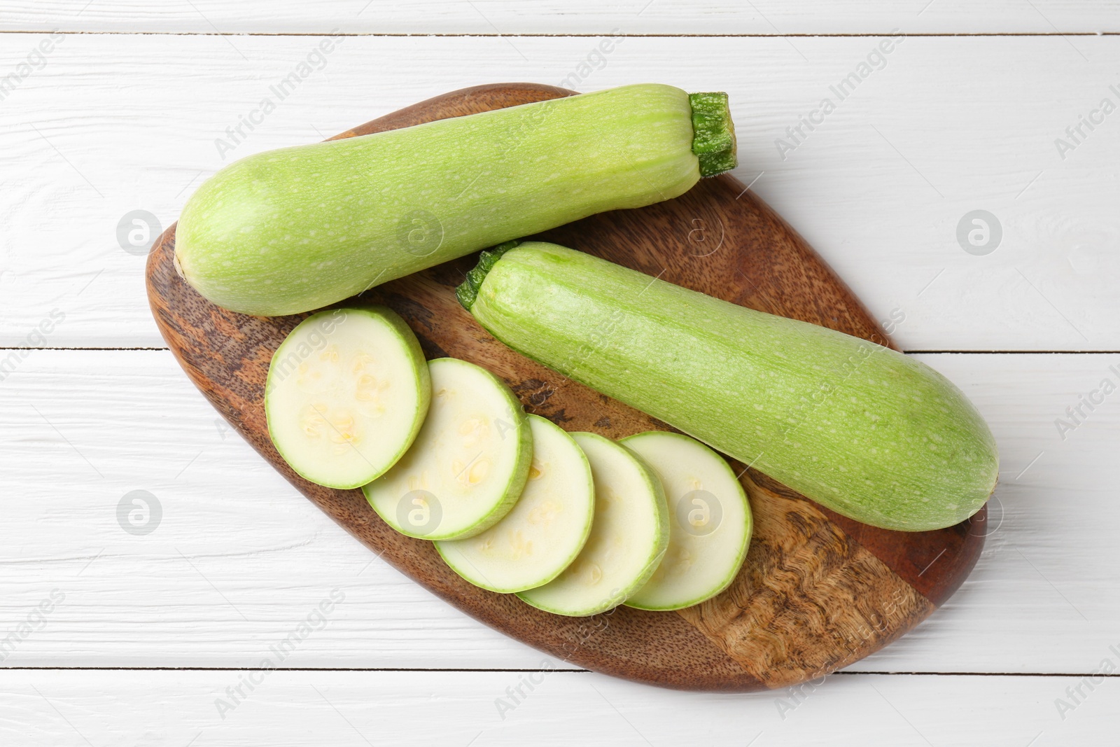 Photo of Board with fresh zucchinis on white wooden table, top view