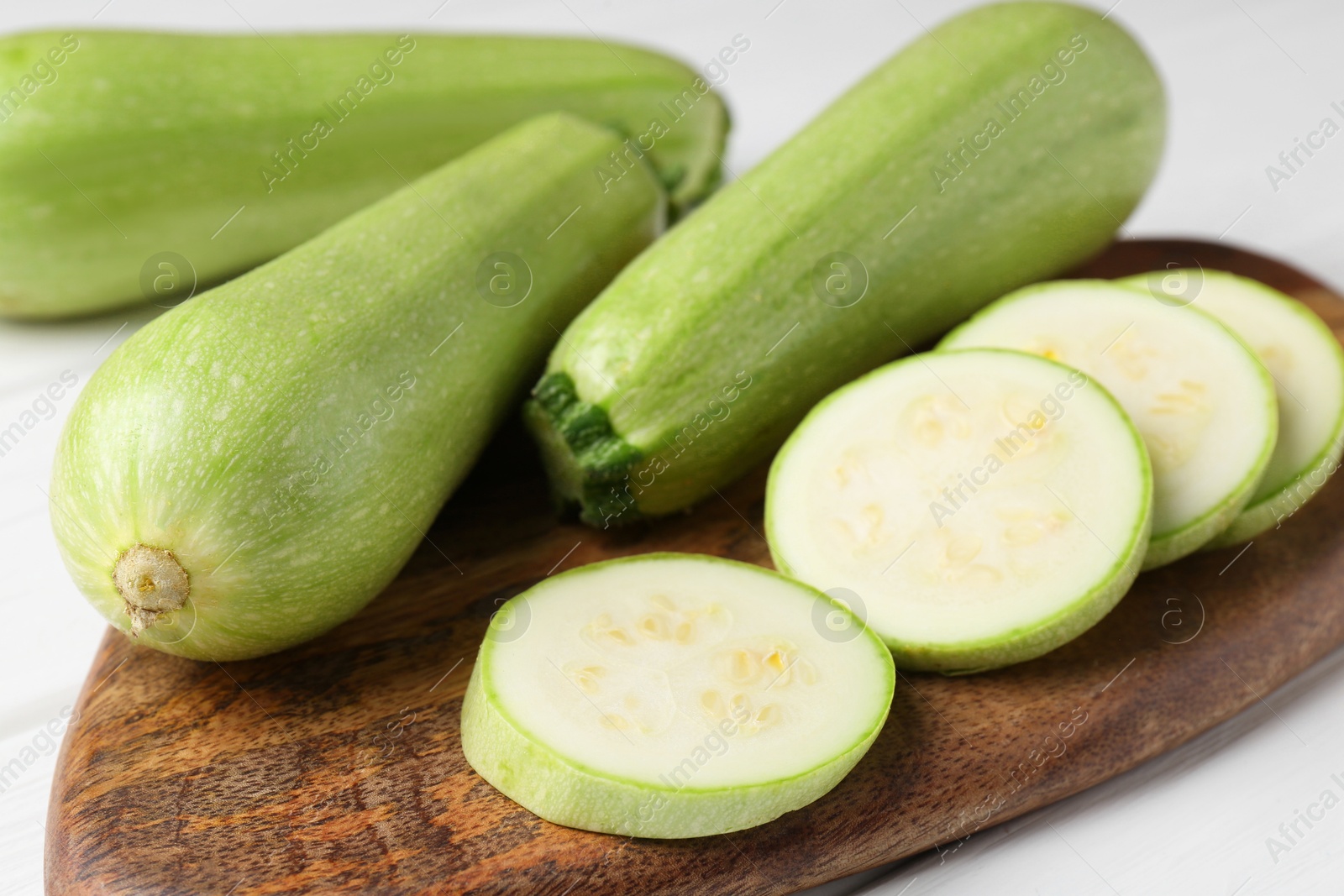 Photo of Board with fresh zucchinis on white table, closeup