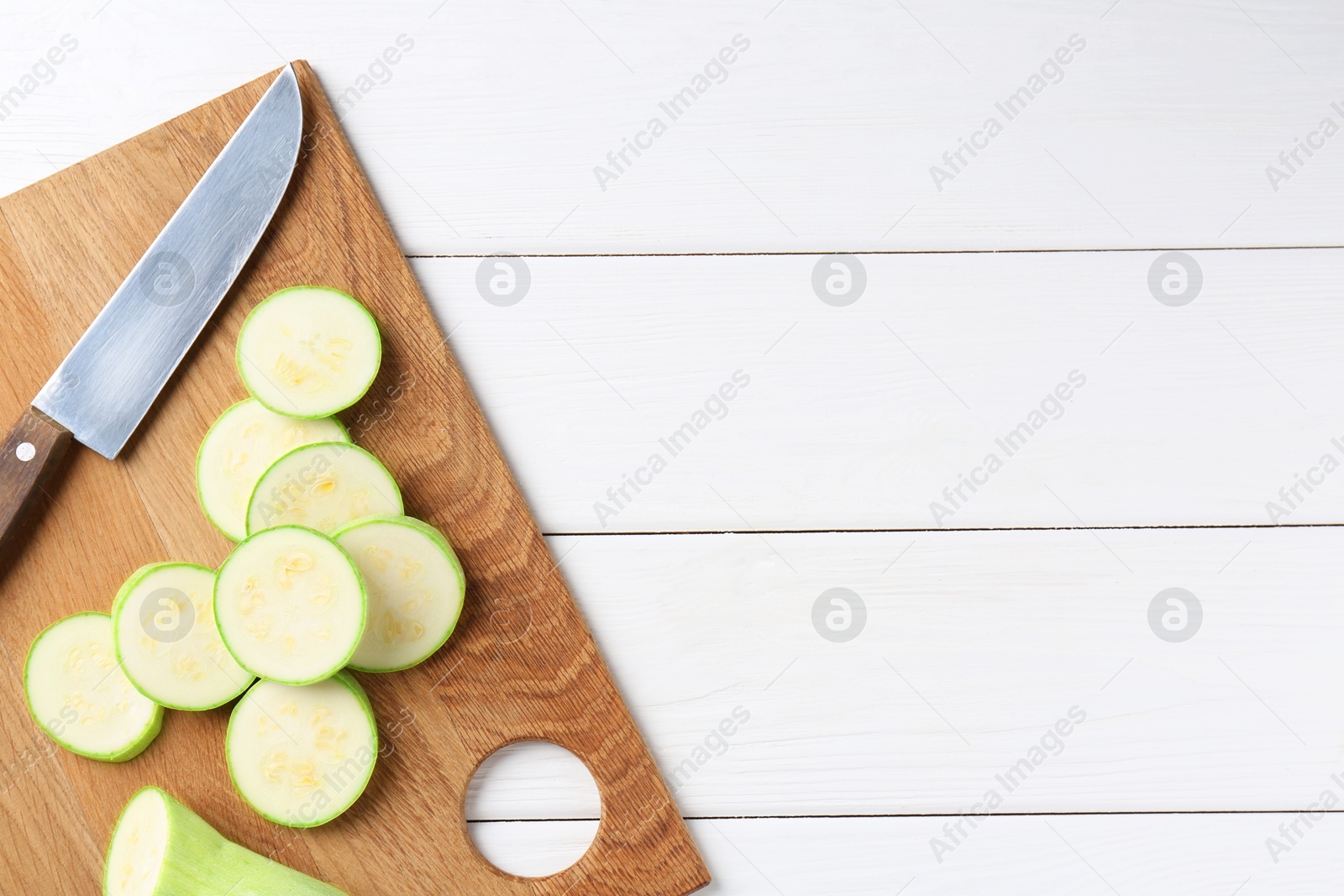 Photo of Board with fresh cut zucchini and knife on white wooden table, top view. Space for text