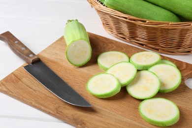 Photo of Board with fresh cut zucchini and knife on white wooden table, closeup