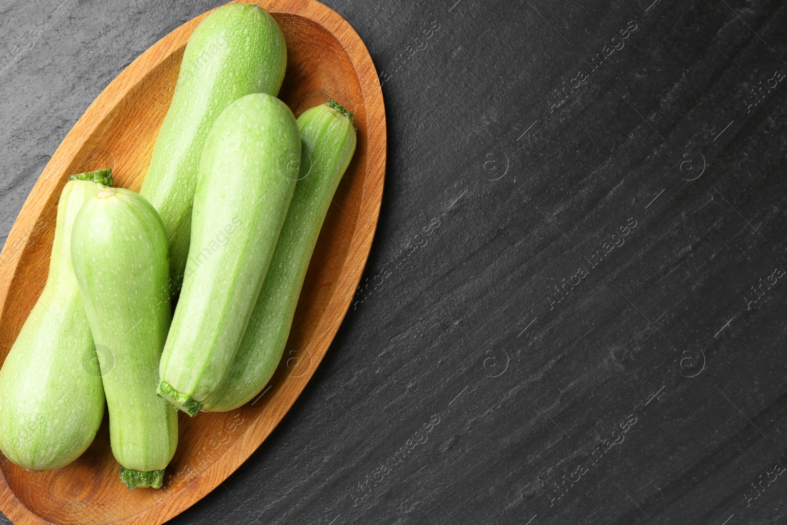 Photo of Fresh zucchinis on dark textured table, top view. Space for text