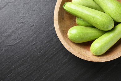 Photo of Fresh zucchinis in bowl on dark textured table, top view. Space for text