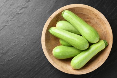 Photo of Fresh zucchinis in bowl on dark textured table, top view. Space for text