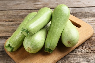 Photo of Board with fresh zucchinis on wooden table, closeup