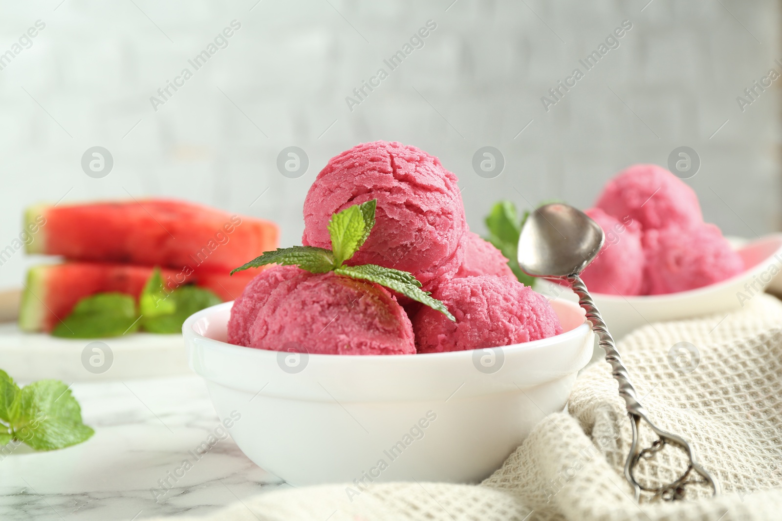 Photo of Scoops of tasty watermelon sorbet with mint in bowl and spoon on white marble table, closeup