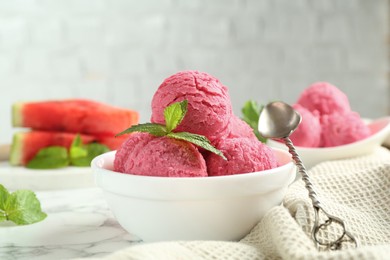 Photo of Scoops of tasty watermelon sorbet with mint in bowl and spoon on white marble table, closeup