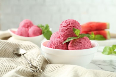 Photo of Scoops of tasty watermelon sorbet with mint in bowls and spoon on white marble table, closeup