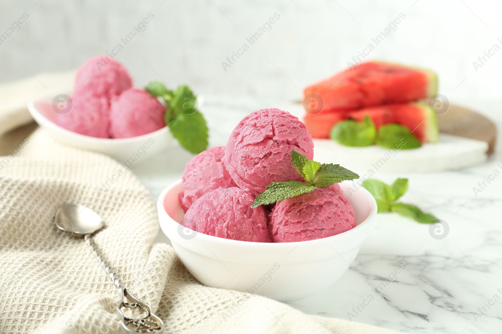 Photo of Scoops of tasty watermelon sorbet with mint in bowls and spoon on white marble table