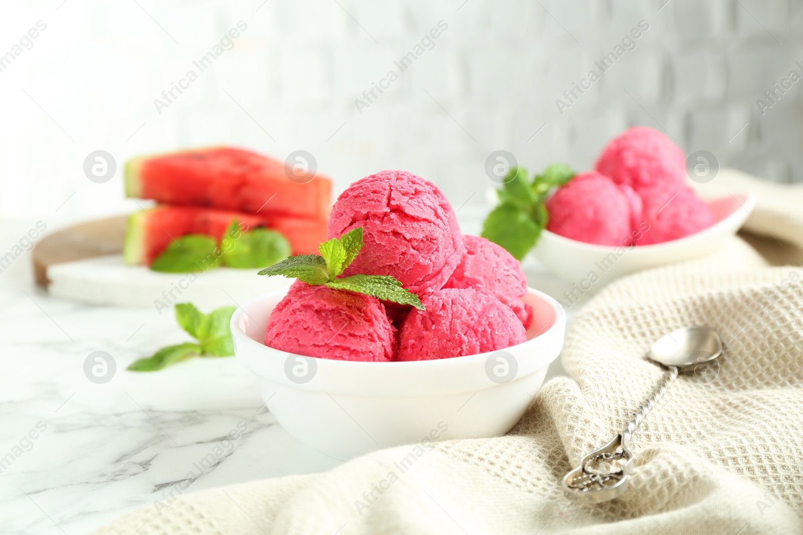 Photo of Scoops of tasty watermelon sorbet with mint in bowls and spoon on white marble table