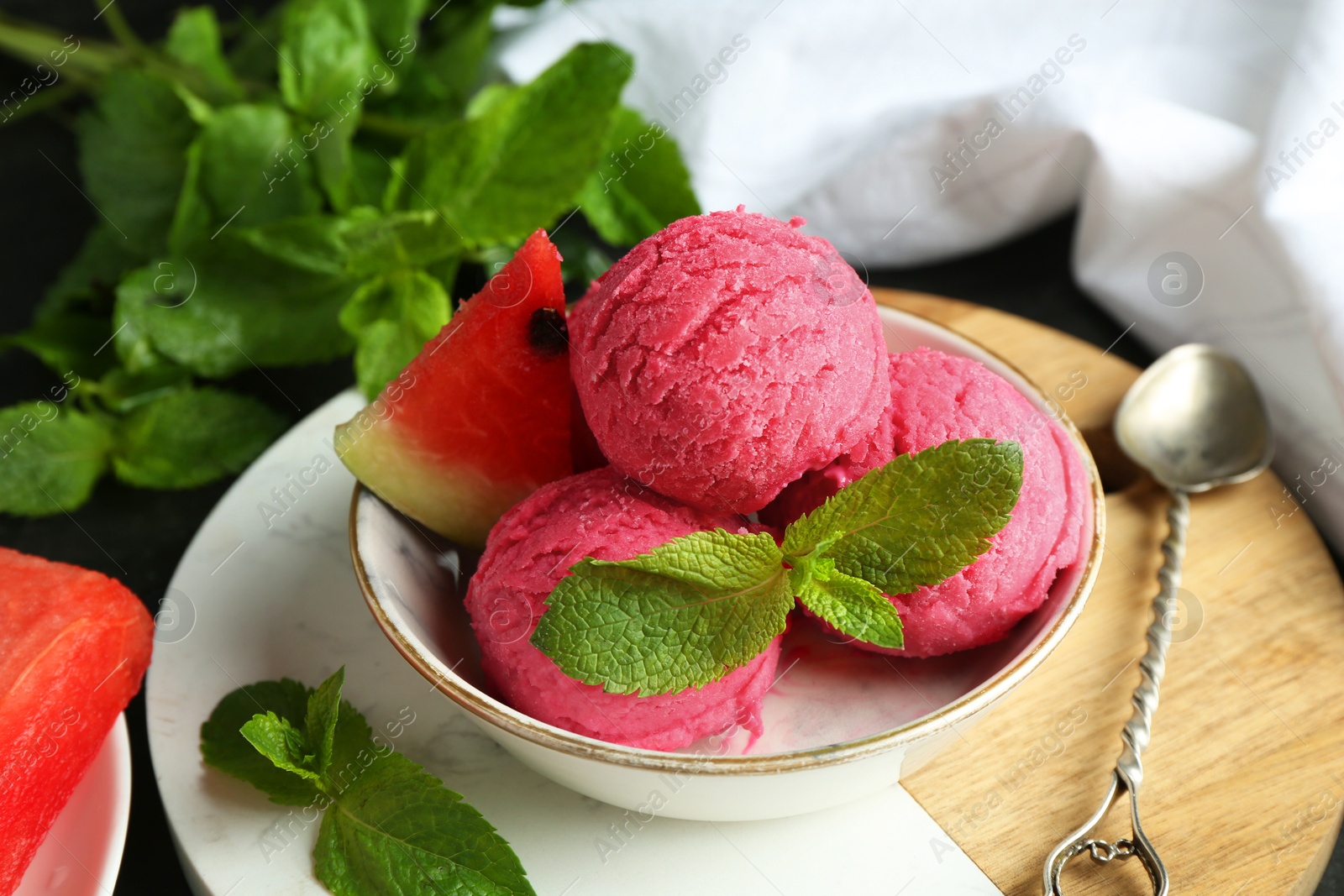 Photo of Scoops of tasty watermelon sorbet with mint, fresh fruit in bowl and spoon on grey table