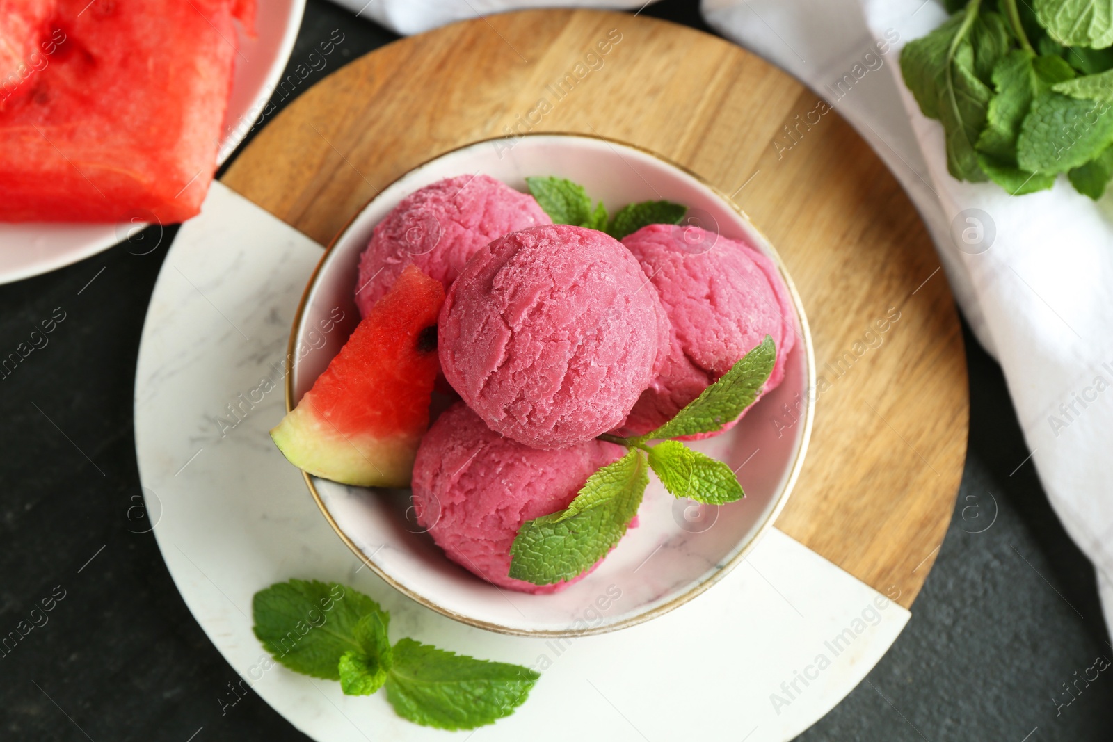 Photo of Scoops of tasty watermelon sorbet with mint and fresh fruit in bowl on grey textured table, flat lay