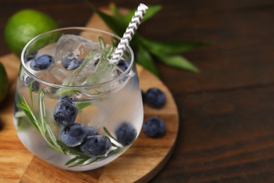 Photo of Refreshing water with blueberries and rosemary in glass on wooden table, closeup. Space for text