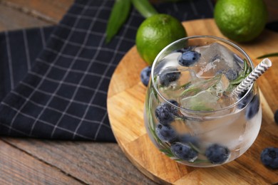 Photo of Refreshing water with blueberries and rosemary in glass on wooden table, closeup. Space for text