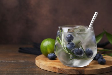 Refreshing water with blueberries and rosemary in glass on wooden table, space for text