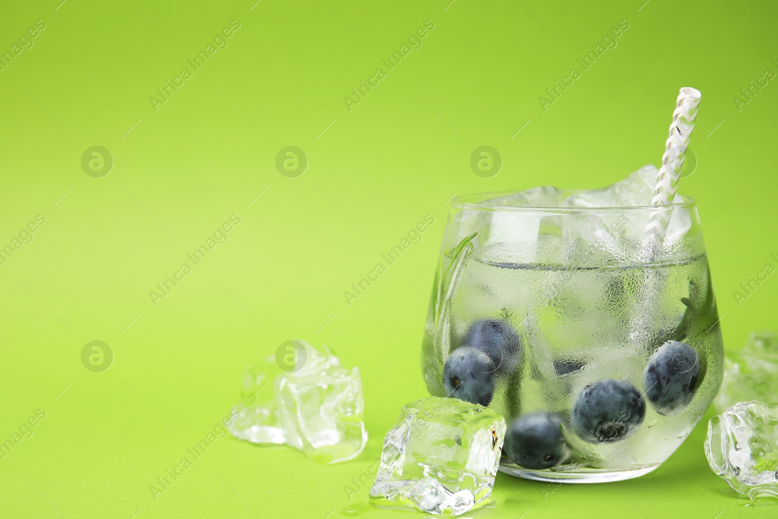 Photo of Refreshing water with blueberries, ice cubes and rosemary on green background, space for text