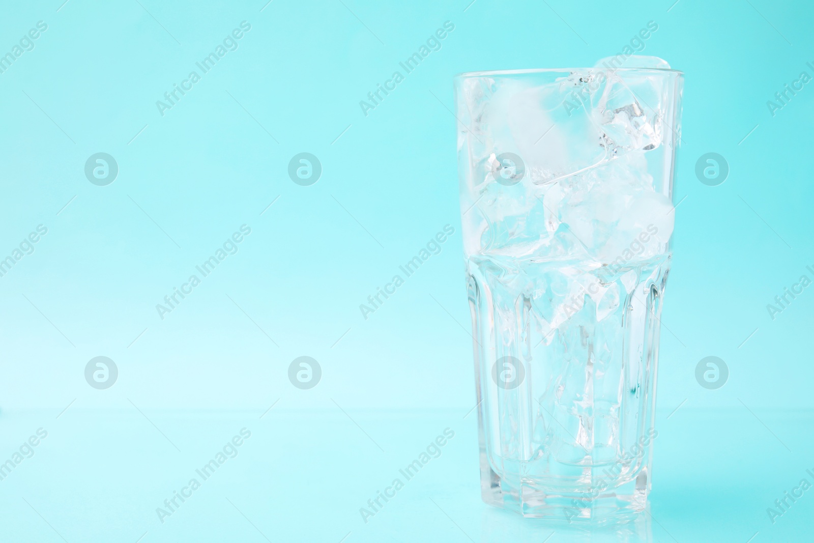 Photo of Refreshing water with ice cubes in glass on light blue background, space for text