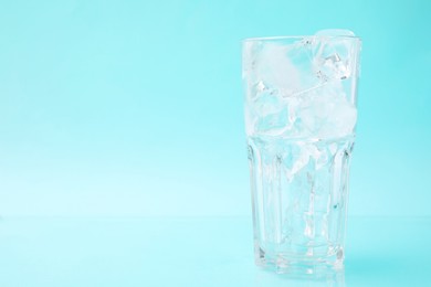 Refreshing water with ice cubes in glass on light blue background, space for text