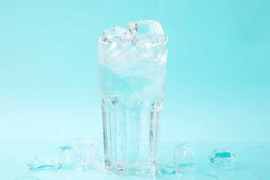 Refreshing water in glass with ice cubes on light blue background